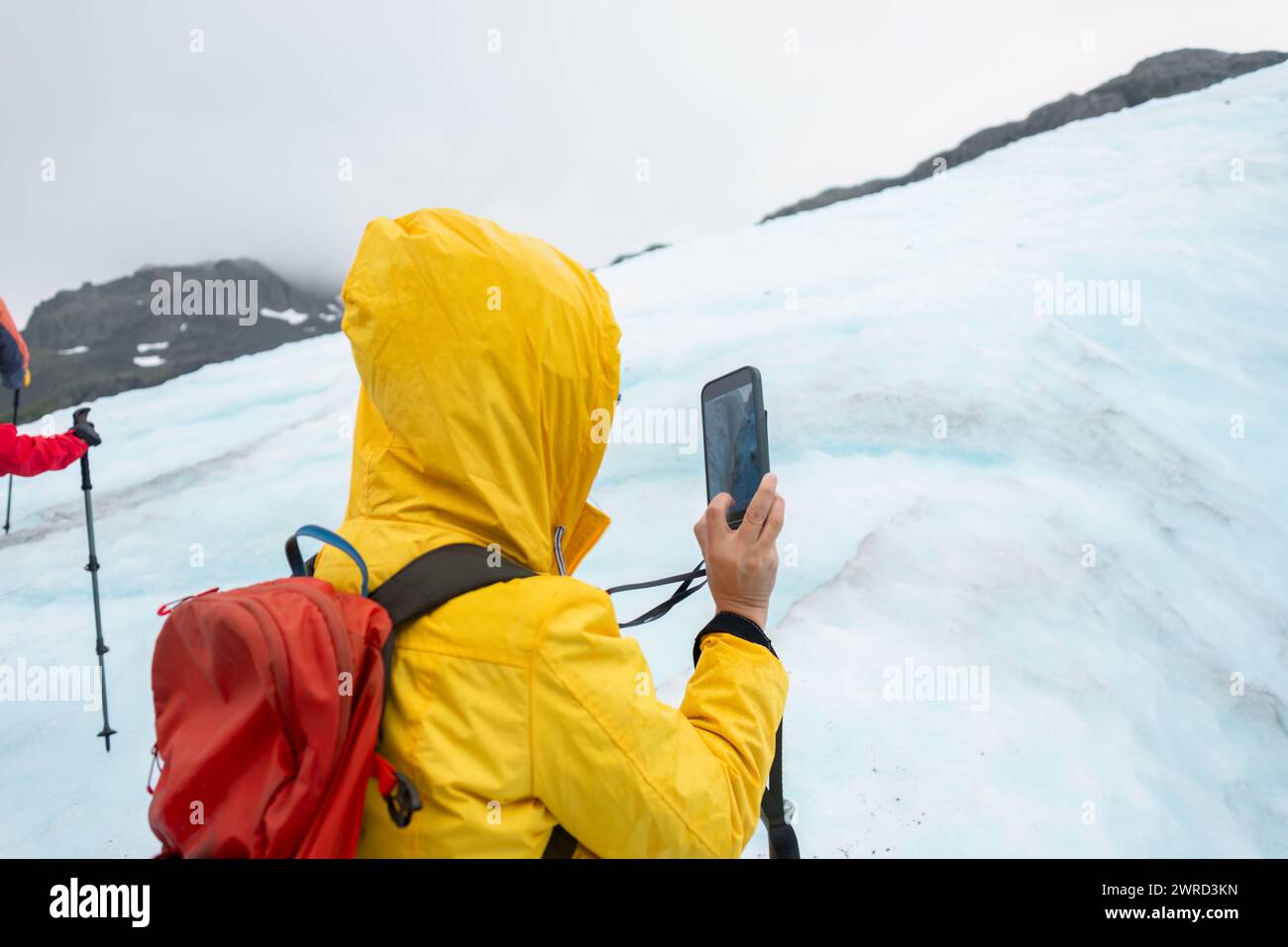 Frau, die Fotos des Gletschers mit dem Smartphone auf dem Exit Glacier macht. Nicht erkennbare Menschen, die im Hintergrund wandern. Kenai Fjords National Park. A Stockfoto