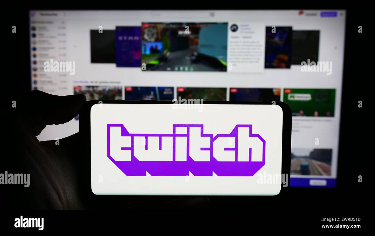 Person, die ein Mobiltelefon mit dem Logo des US-amerikanischen Live-Streaming-Unternehmens Twitch Interactive Inc. Vor der Webseite des Unternehmens hält. Schwerpunkt auf dem Display des Telefons. Stockfoto