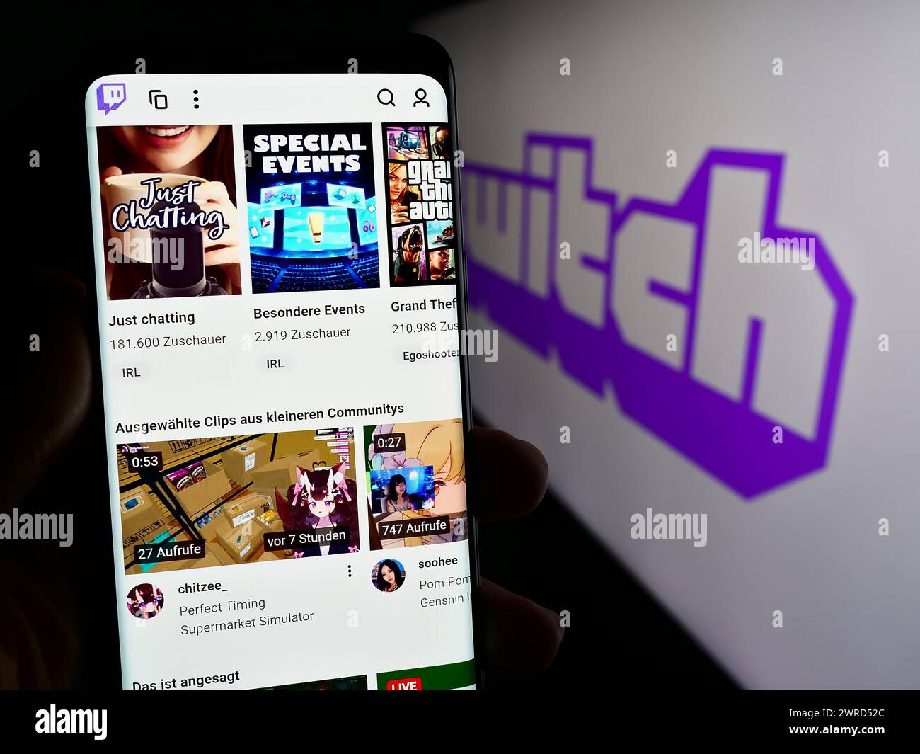 Person, die ein Mobiltelefon hält, mit Webseite des US-amerikanischen Live-Streaming-Unternehmens Twitch Interactive Inc. Vor dem Logo. Konzentrieren Sie sich auf die Mitte des Telefondisplays. Stockfoto