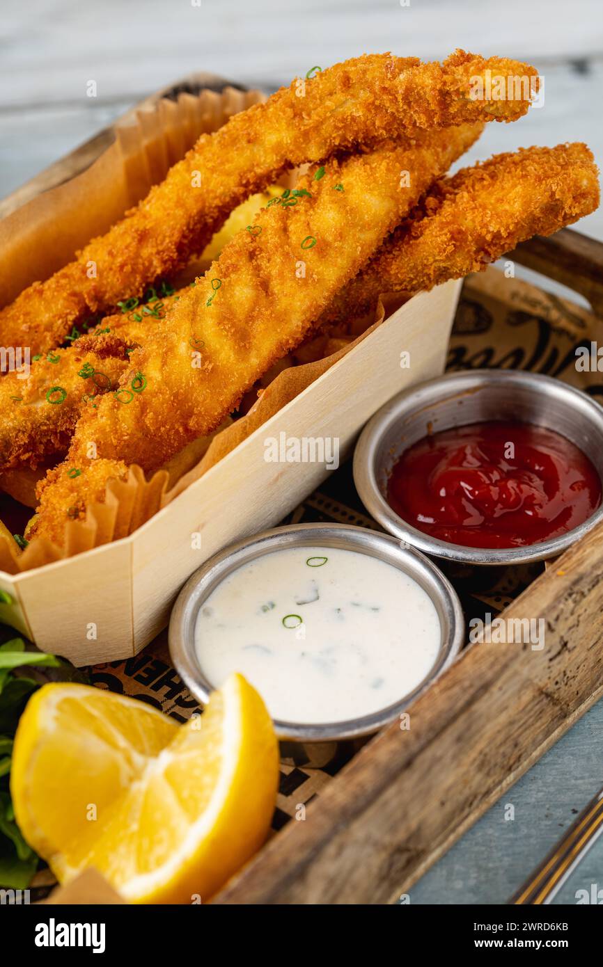 Fish and Chips mit frischem Gemüse und Saucen auf Holztisch Stockfoto