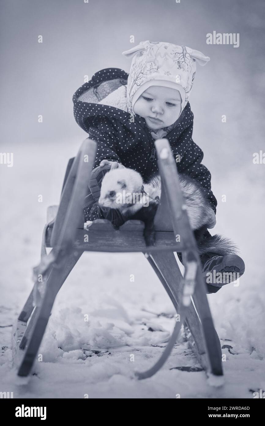 Ein Jahr altes Baby auf Holzrodelbahn mit Frettchenfreund Stockfoto