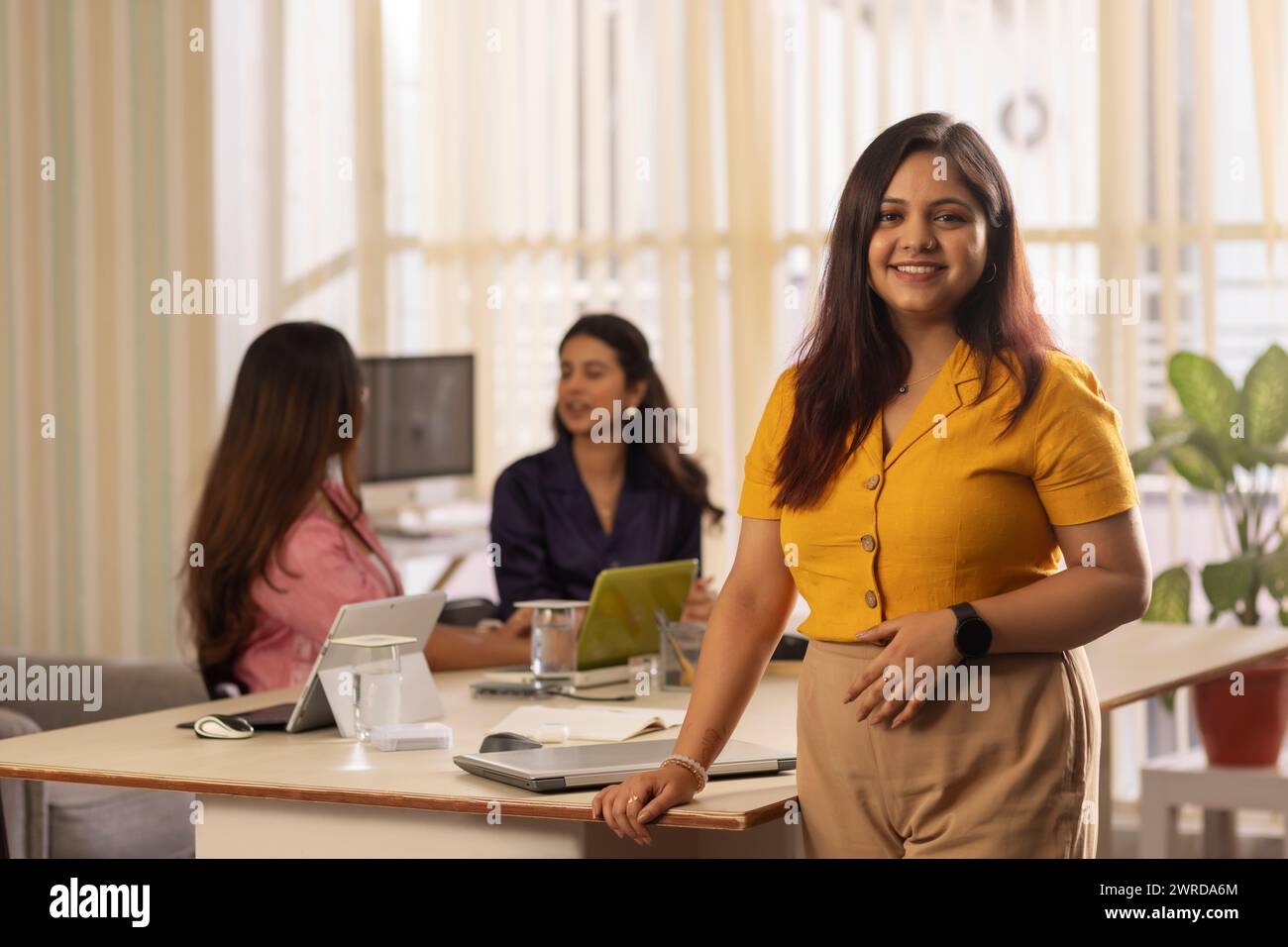 Porträt einer jungen Geschäftsfrau, die in einem Büro mit ihren Kollegen im Hintergrund steht Stockfoto