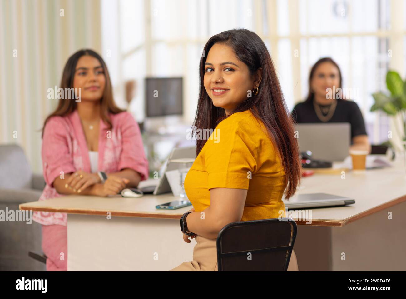 Porträt einer jungen Geschäftsfrau, die in einem Büro sitzt, mit ihren Kollegen im Hintergrund Stockfoto