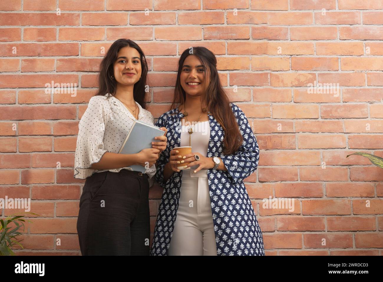 Porträt von zwei lächelnden Geschäftsfrauen, die stehen und die Kamera vor einer Ziegelwand betrachten Stockfoto