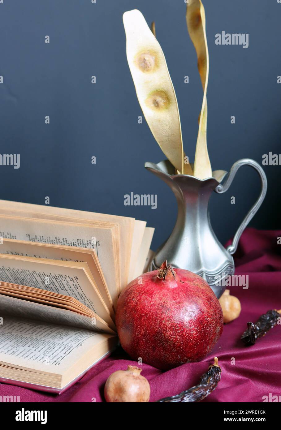 Stillleben mit Granatapfel, Buch und Silbervase. Dunkelgrauer Hintergrund mit Kopierraum. Lesekonzept. Stockfoto