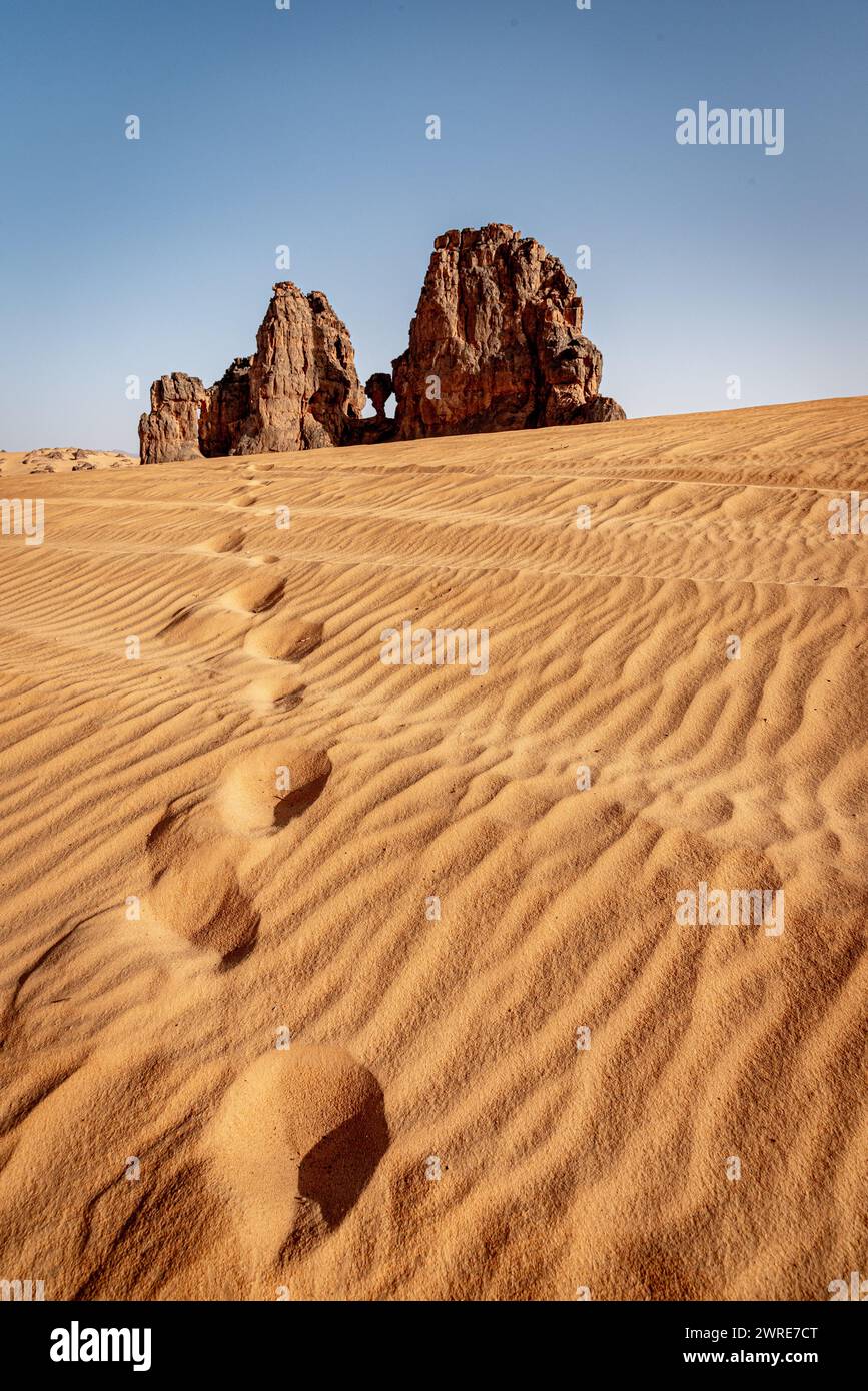 Landschaft von Erg Admer in der Sahara, Algerien. Fußspuren führen zu einer Felsformation am Standort der Cying Cow Stockfoto