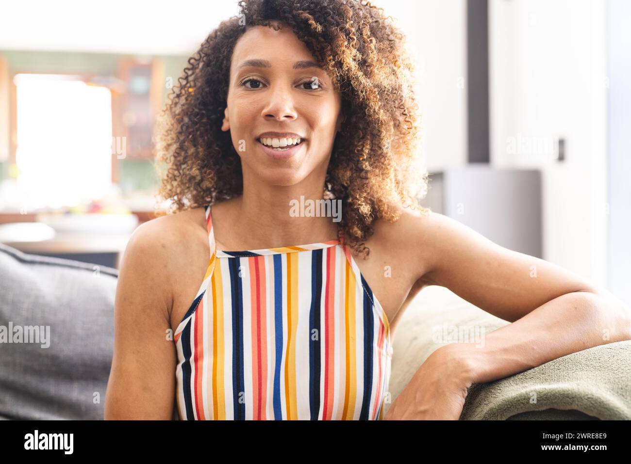 Birassische Frau mit lockigen braunen Haaren lächelt warm und trägt ein bunt gestreiftes Oberteil Stockfoto