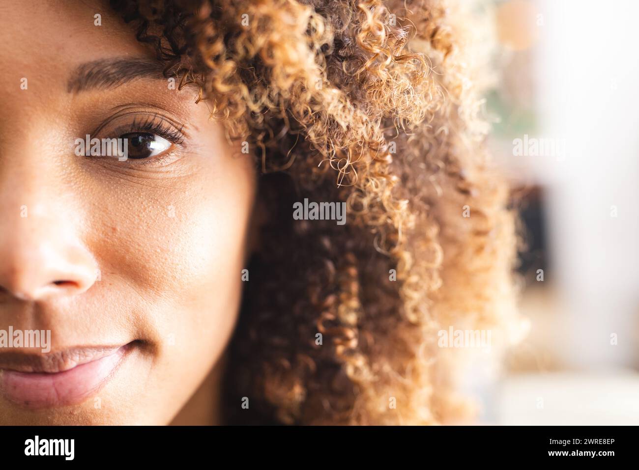 Nahaufnahme einer zweirassigen Frau mit lockigem Haar und warmbraunen Augen Stockfoto