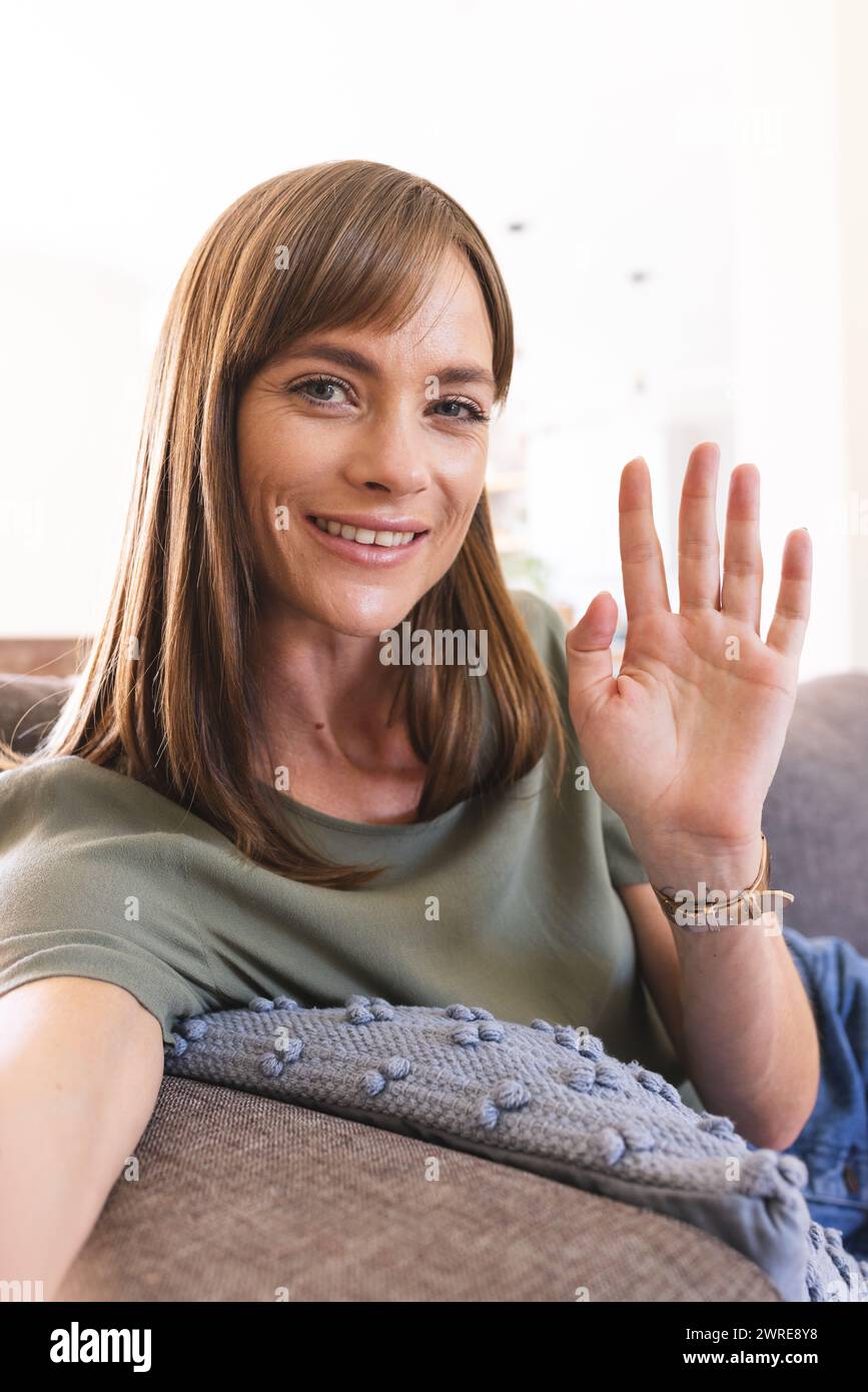 Kaukasische Frau mit braunen Haarwellen vor der Kamera auf Videoanruf, bequem zu Hause Stockfoto