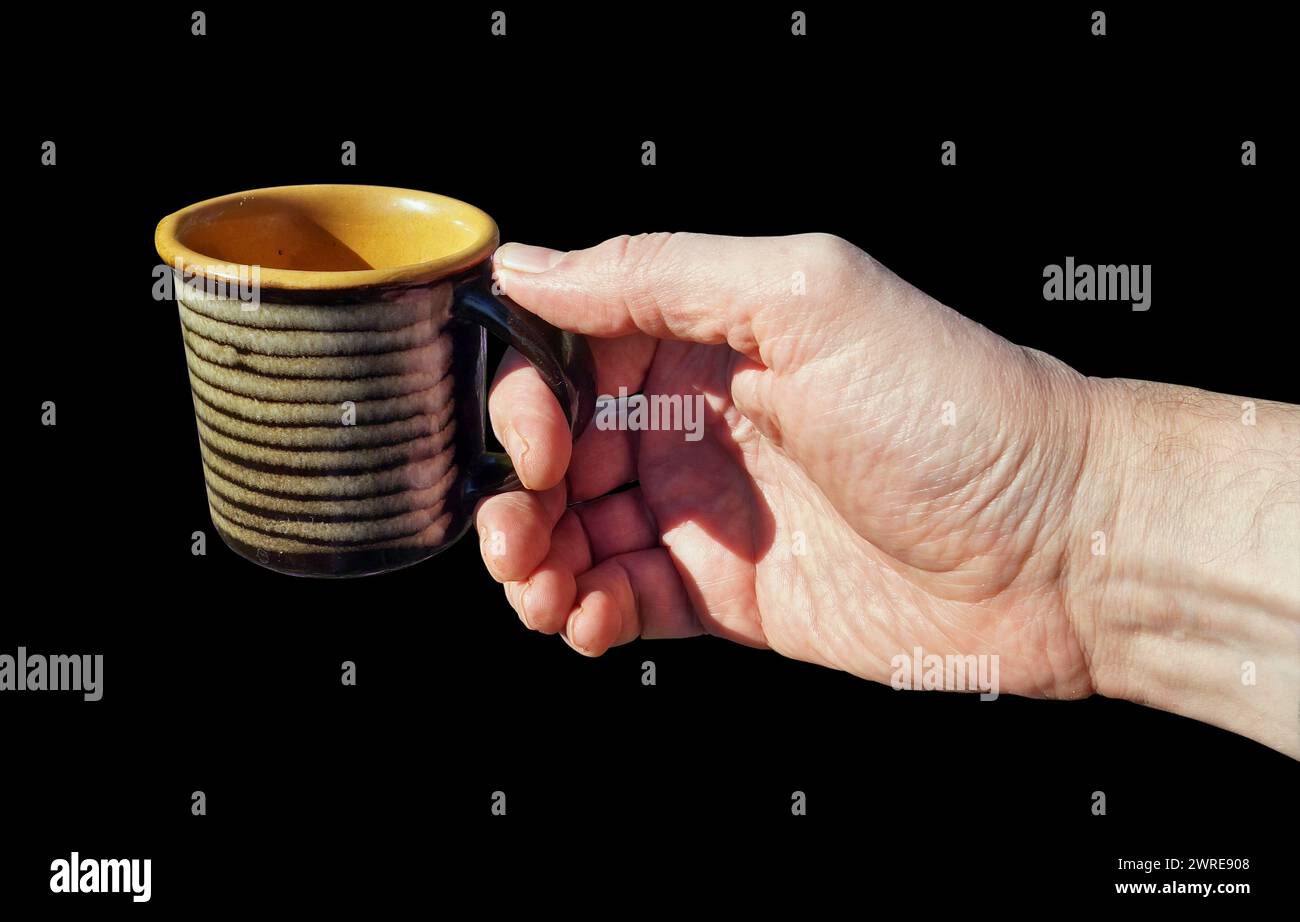 Ein Mann hält einen leeren Keramikbecher in der Hand. Isoliert auf Schwarz Stockfoto