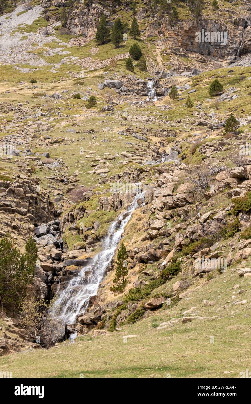 Ruhige Berglandschaft mit einem kaskadierenden Wasserfall, der durch zerklüftetes, felsiges Gelände in kargem Grün fließt Stockfoto