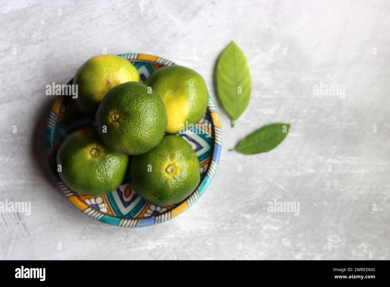 Einfache Kompositionen Stillleben mit grünen Limetten auf einer blauen Keramikplatte. Hellgrauer Hintergrund mit Platz für Text. Konzept für gesunde Ernährung. Stockfoto