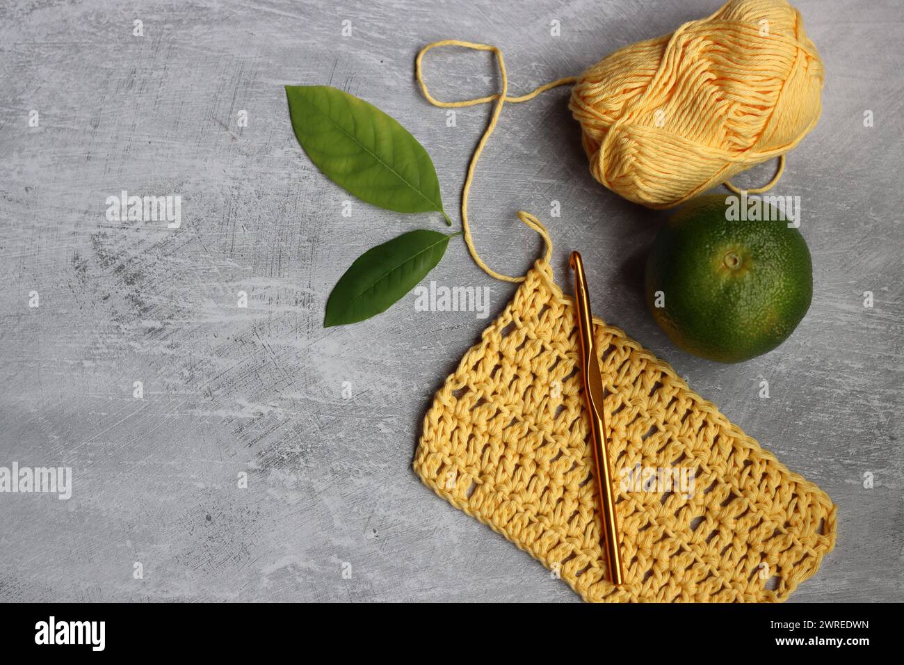Gelbes Häkelprojekt. Garn aus Bio-Baumwolle auf grauem Hintergrund mit Kopierraum Stockfoto