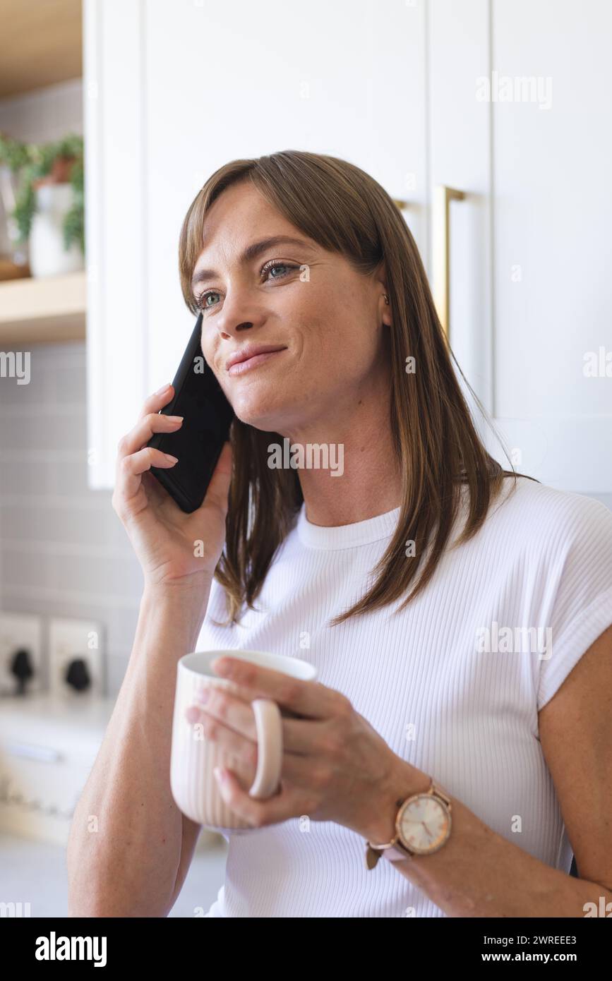 Eine weiße Frau spricht am Telefon, während sie einen weißen Becher hält Stockfoto