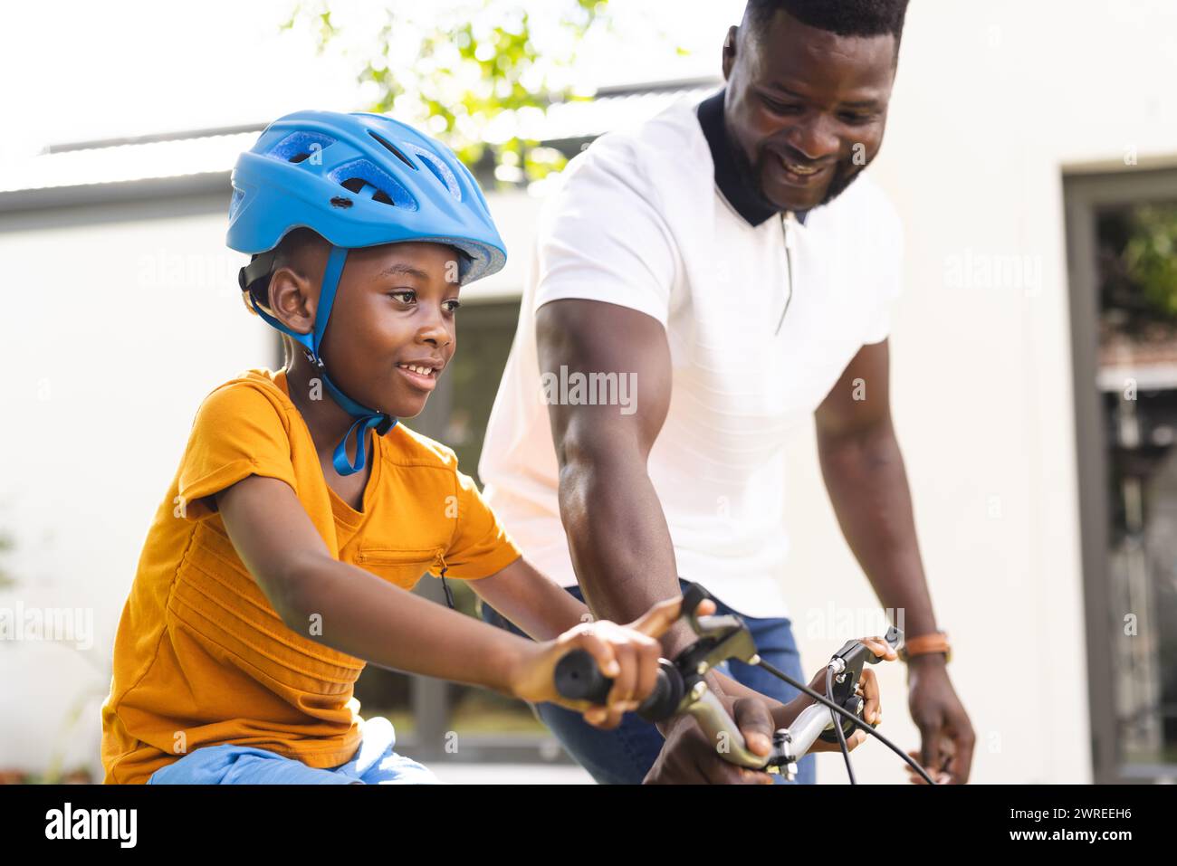 Der afroamerikanische Vater bringt seinem Sohn das Fahrradfahren im Garten bei, beide lächeln fröhlich Stockfoto