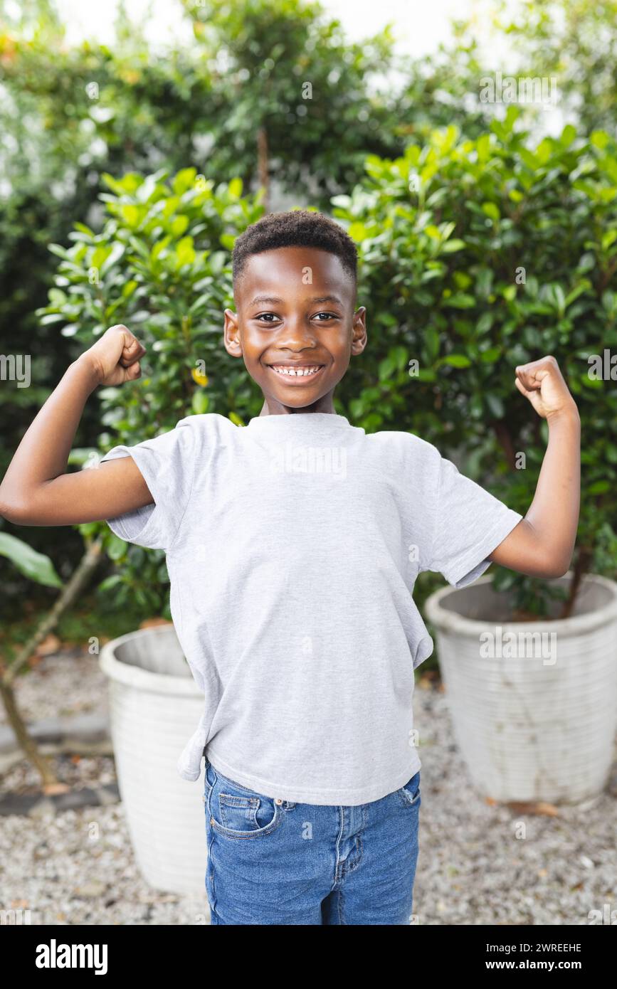 Der afroamerikanische Junge spannt seine Muskeln mit einem hellen Lächeln in einem Garten Stockfoto