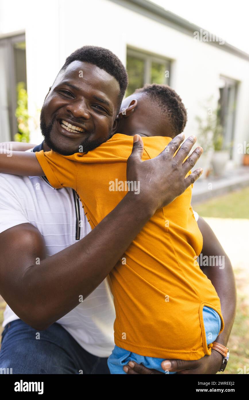 Der afroamerikanische Vater umarmt seinen Sohn, beide lächeln fröhlich im Hinterhof Stockfoto