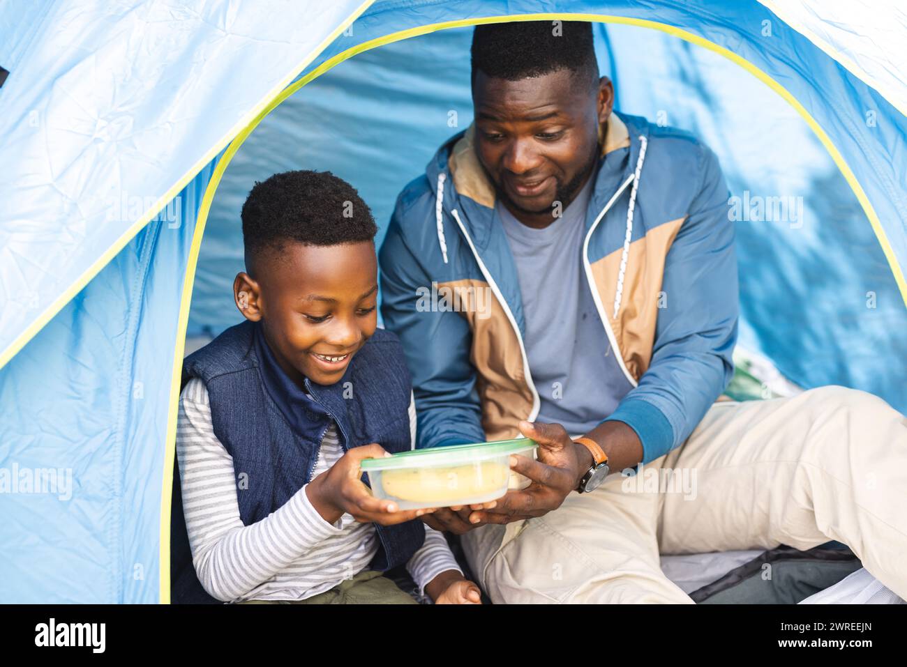 Afroamerikaner Vater und Sohn teilen sich einen Moment in einem Zelt und halten einen Container Stockfoto