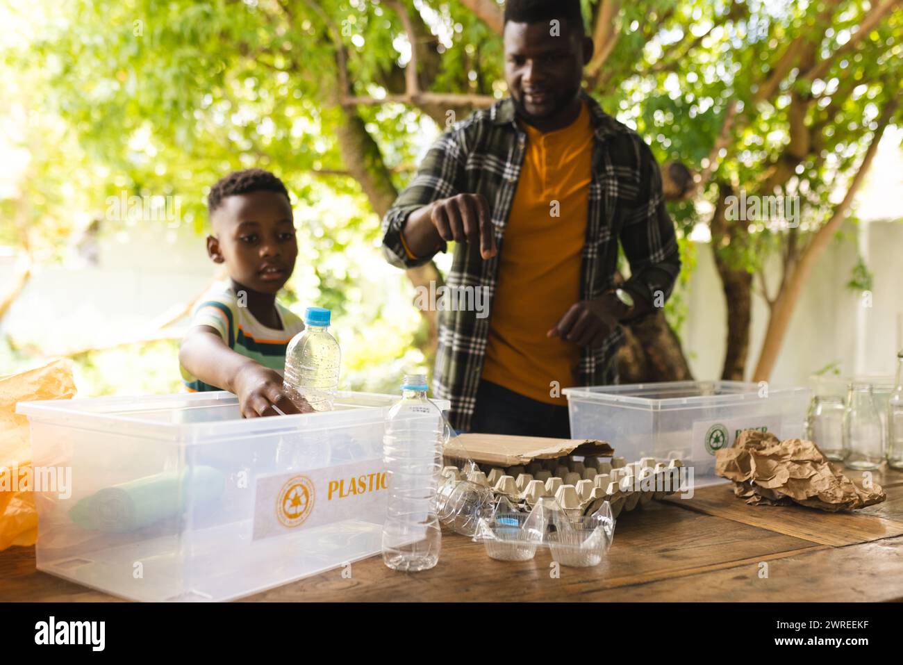 Afroamerikanischer Vater und Sohn sortieren im Freien Wertstoffe und setzen Umweltwerte ein Stockfoto
