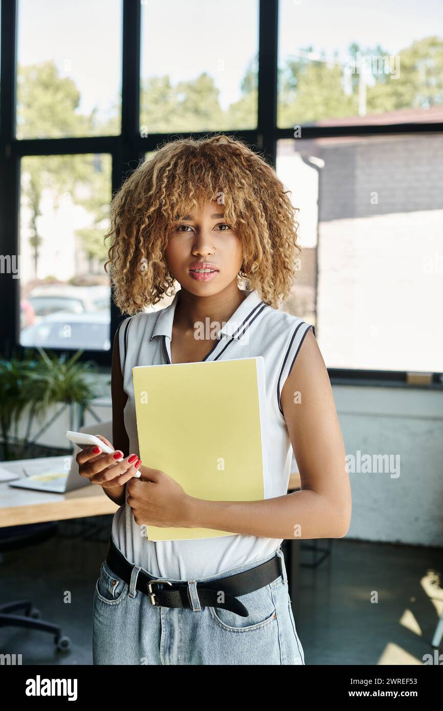 Lockiger afroamerikanischer Unternehmer in Zahnspangen, der Dokumente und Smartphone im Büro hält Stockfoto