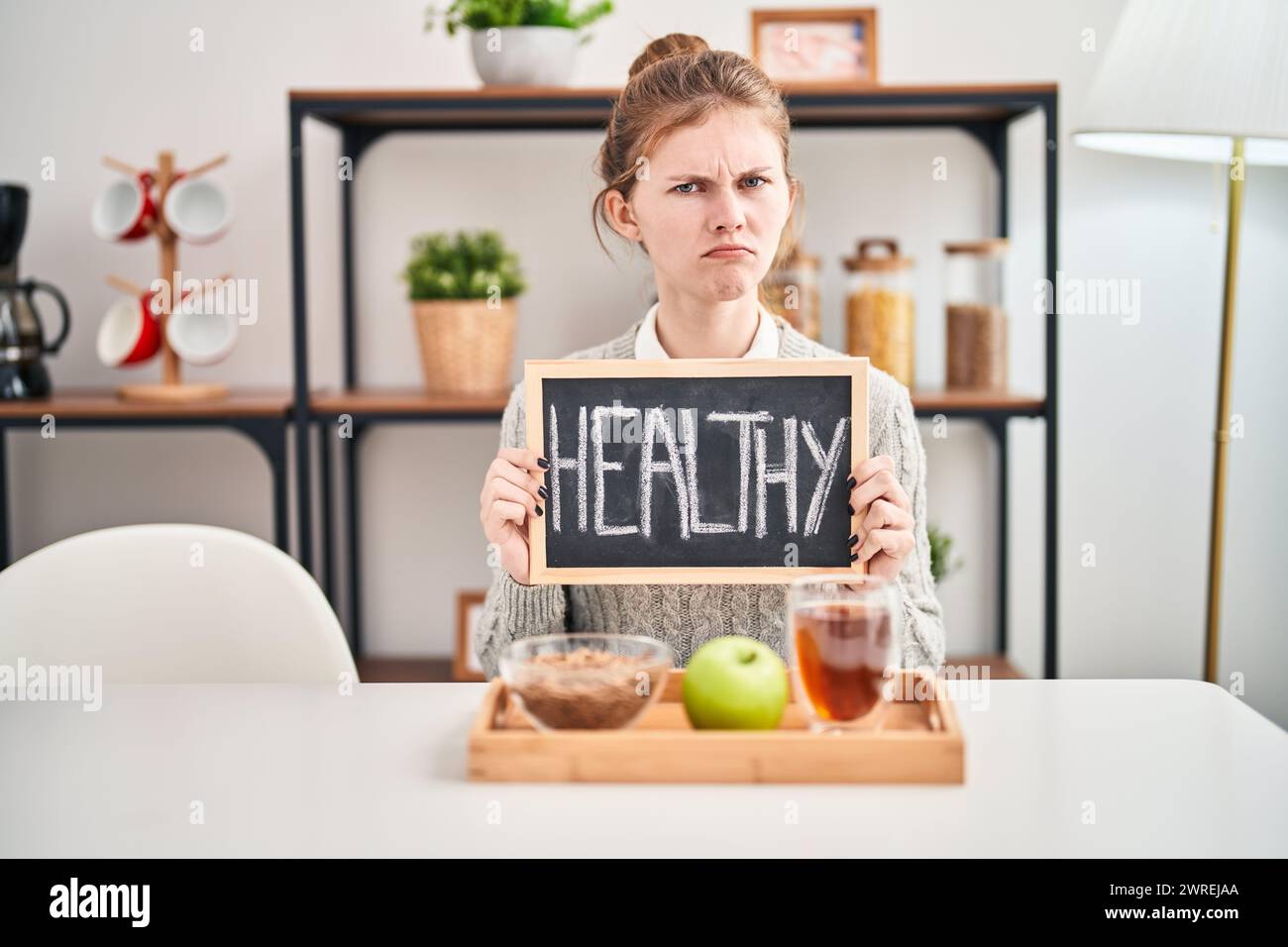 Runzelnde junge blonde Frau mit Problemen, skeptisch und nervös beim Genießen eines gesunden Frühstücks zu Hause, eindeutig verärgert. Stockfoto