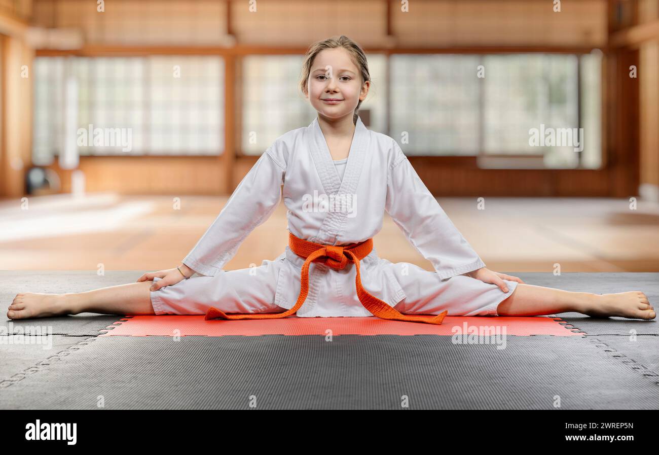 Fröhliches Kind in Karate-Uniform macht einen Spalt auf einer Matte Stockfoto