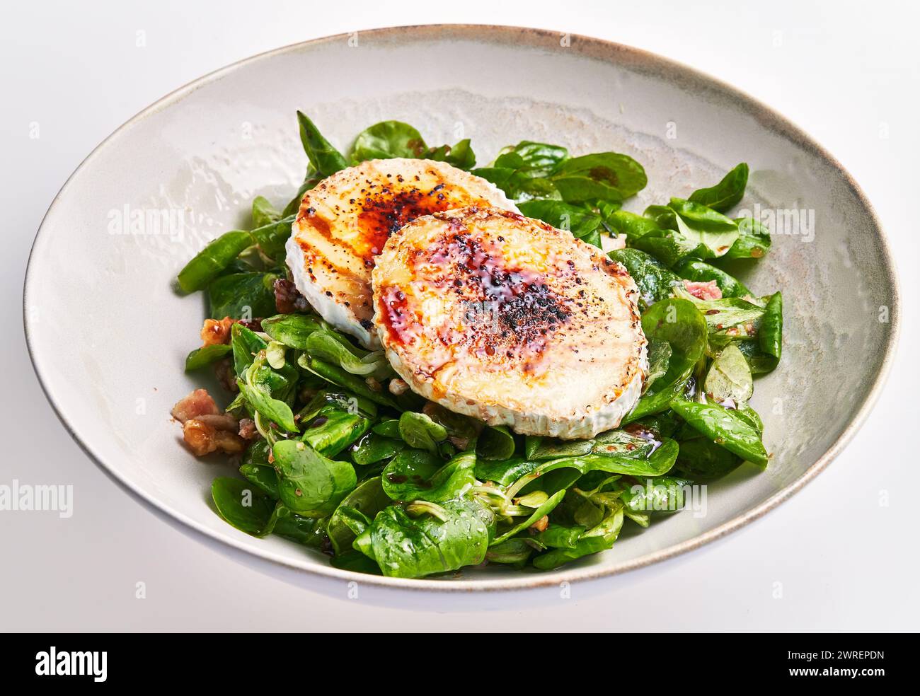 Gegrillter Ziegenkäse auf einem Bett mit frischem Spinatsalat in einer Keramikschale, die vegetarische Gourmetküche eingefangen Stockfoto