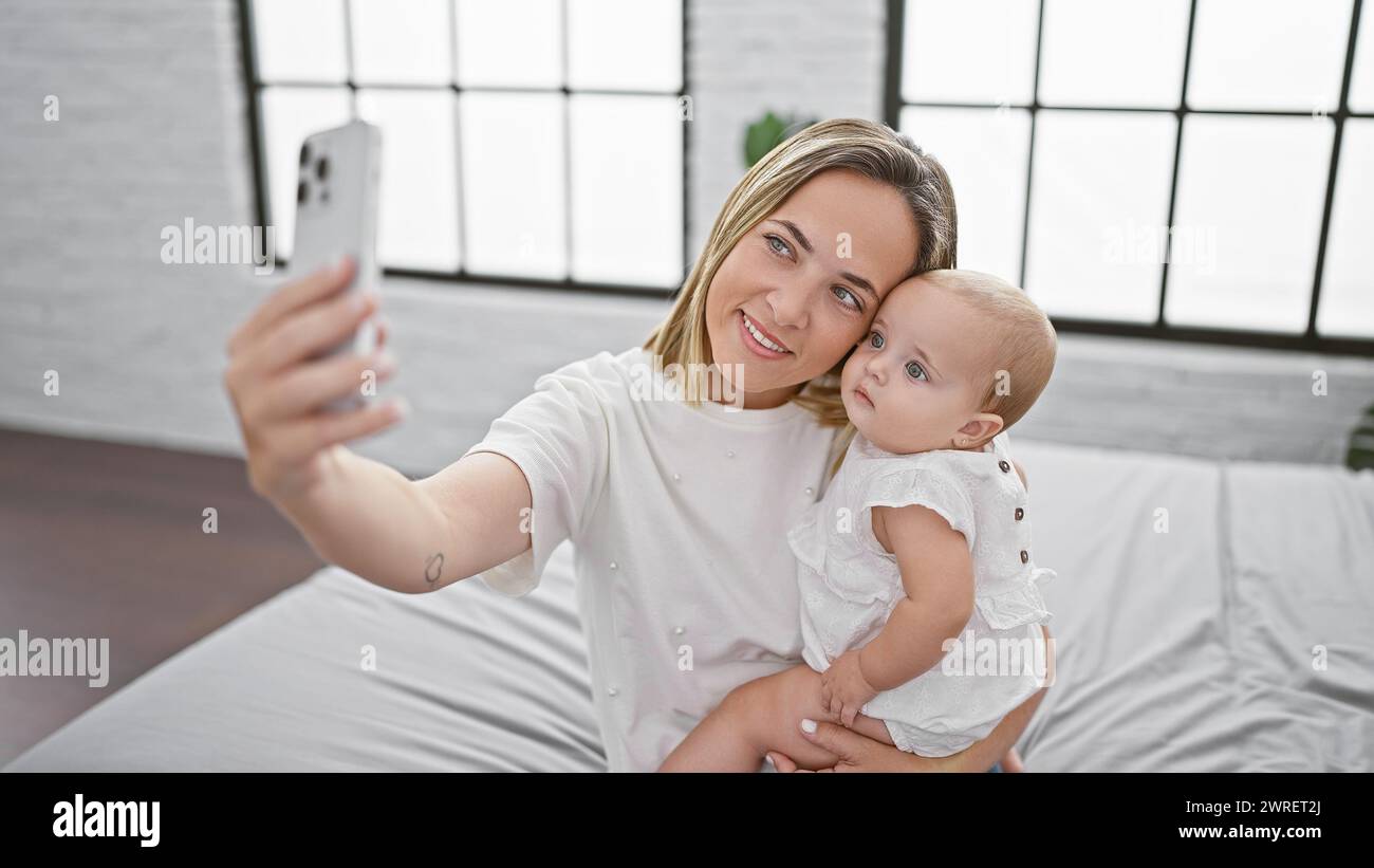 Glückliche Mutter und Tochter machen selbstbewusstes Selfie und fangen wertvolle Momente der Liebe und des Zusammenlebens in dem gemütlichen Zimmer ein, das auf dem Bett sitzt und Bilder macht Stockfoto