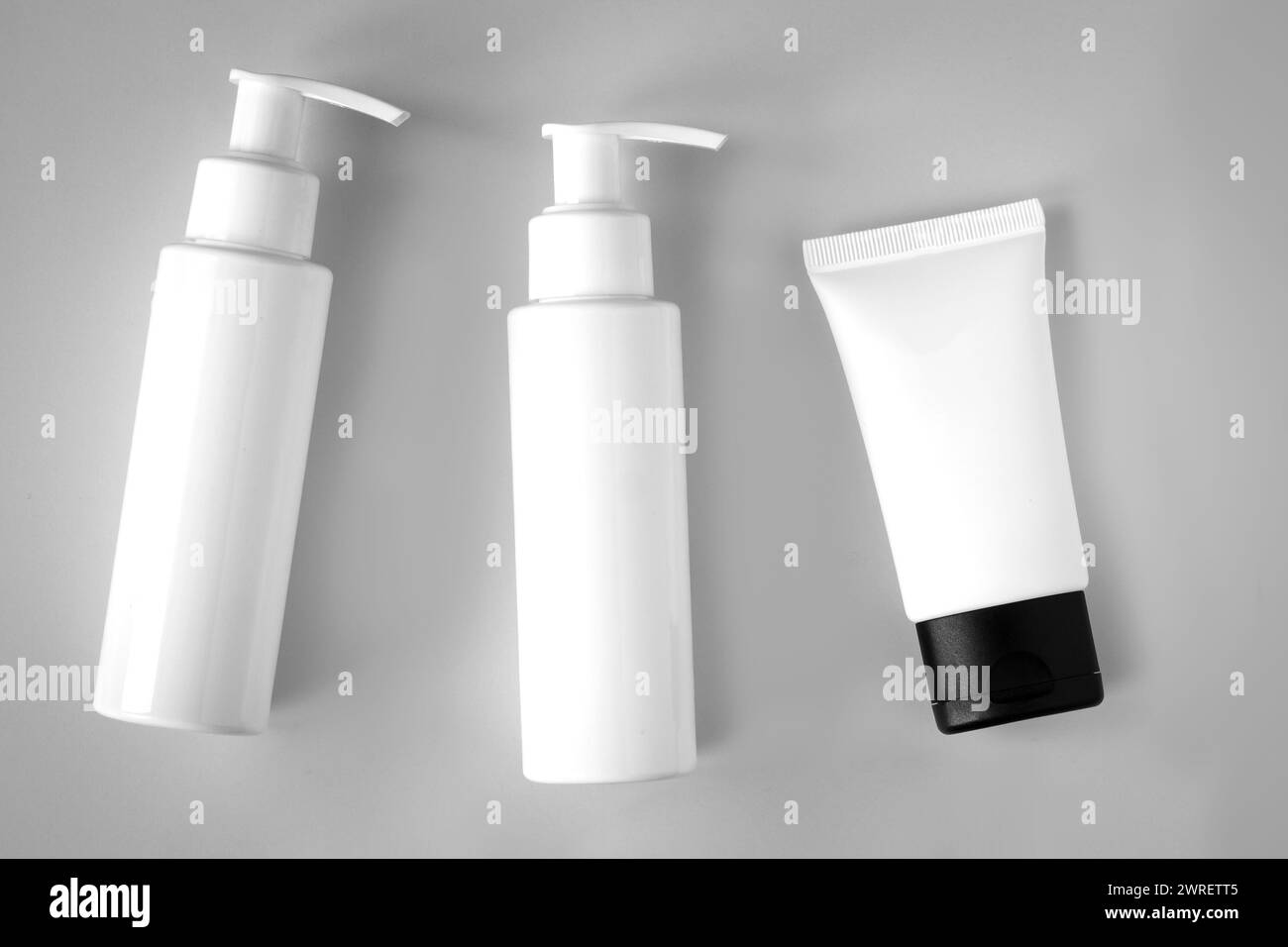 Weiße Flaschen und Röhrchen mit kosmetischen Produkten mit Branding auf grauem Hintergrund. Hautpflege und Schönheitskonzept Stockfoto