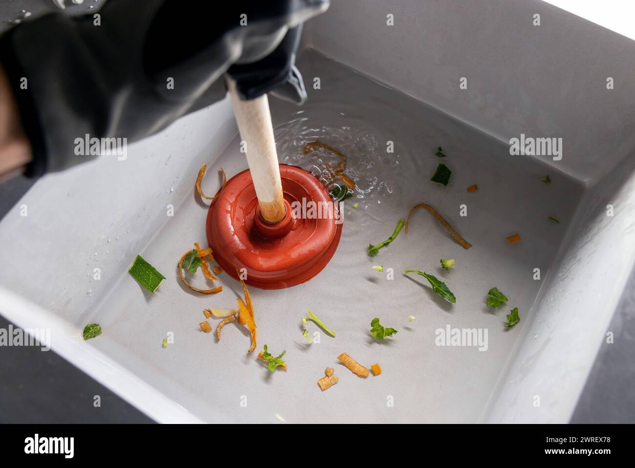 Klempner reinigt verstopfte Küchenspüle mit Kolben Stockfoto