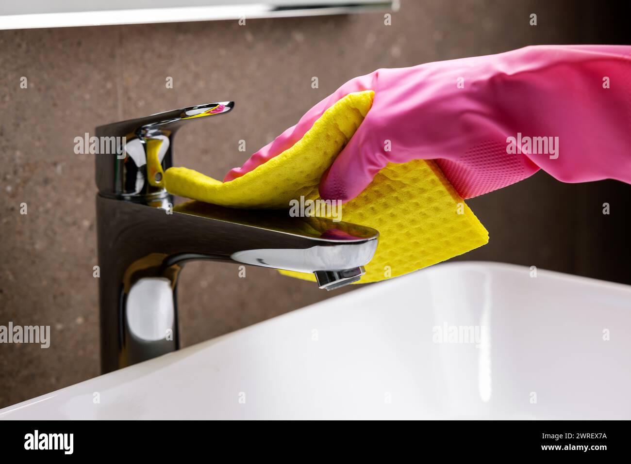 Reinigungsservice und Hausarbeiten. Hand mit Gummihandschuh und Schwamm reinigt den Chromhahn des Waschbeckens im Badezimmer Stockfoto