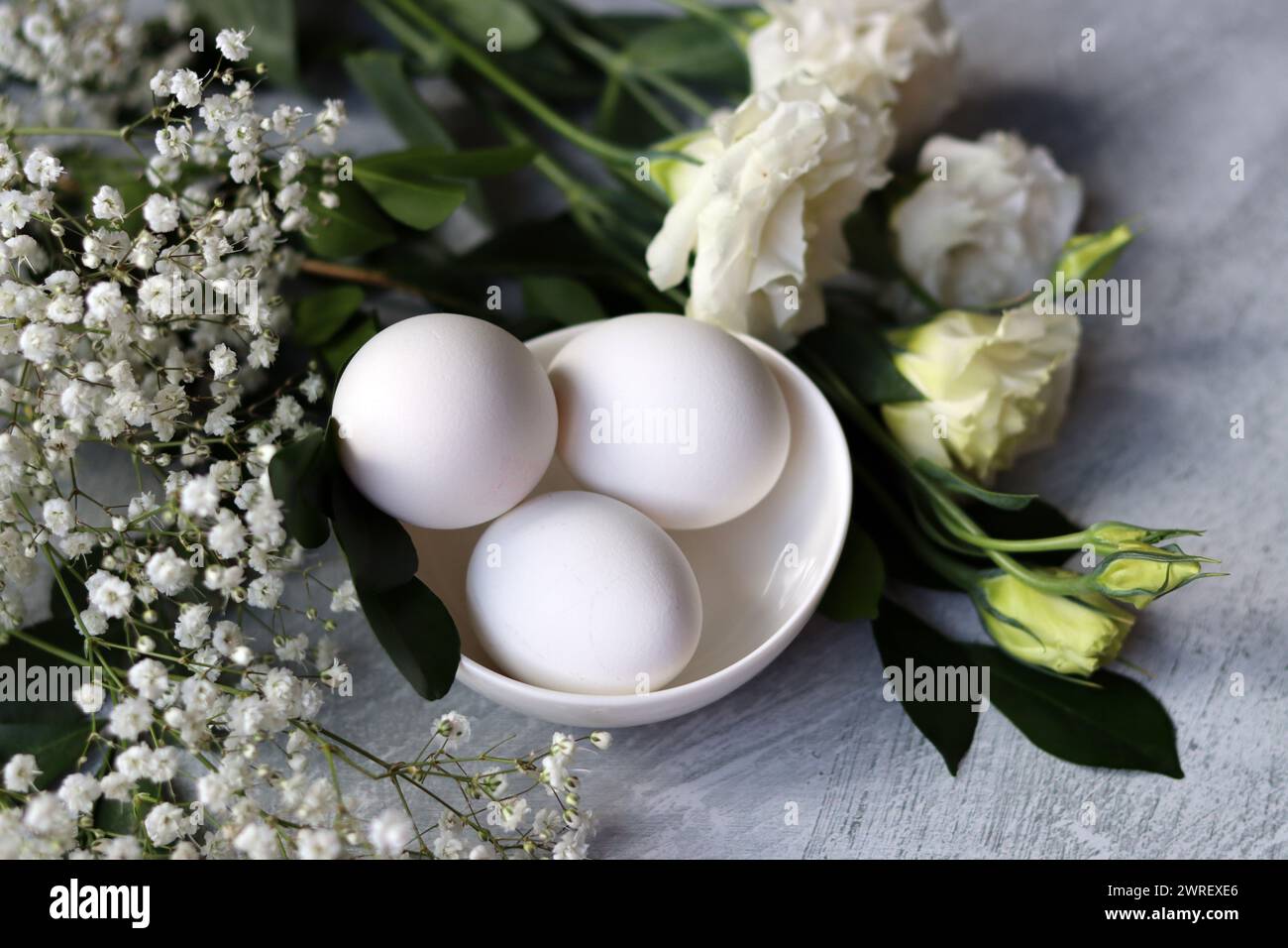 Einfache Komposition Stillleben mit Eiern und weißen Blüten. Osterfest-Konzept. Eier in einer weißen Keramikschale von oben. Stockfoto