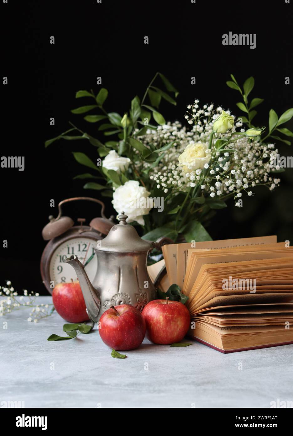 Stillleben-Foto von einem Vintage-Metallteekessel, einem alten Buch und roten Äpfeln auf einem Tisch. Retro-Ästhetik-Konzept. Stockfoto