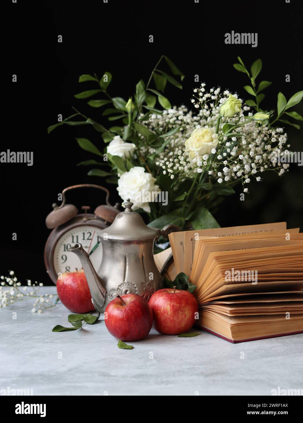 Stillleben-Foto von einem Vintage-Metallteekessel, einem alten Buch und roten Äpfeln auf einem Tisch. Retro-Ästhetik-Konzept. Stockfoto