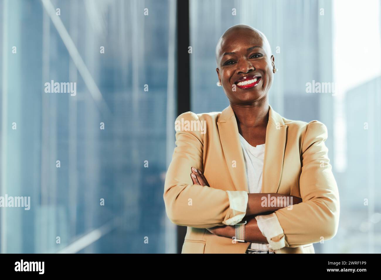Selbstbewusste schwarze Geschäftsfrau steht im Büro mit überkreuzten Armen und stellt Erfolg und Professionalität dar. Sie strahlt Selbstvertrauen und Glück aus Stockfoto