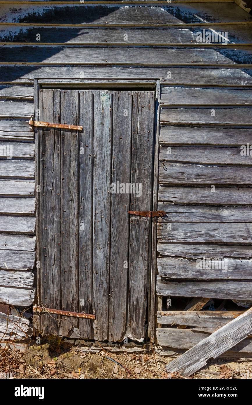 Rustikales Hintergrundbild eines verwitterten und verfaulenden Holzschuppen seine Türscharniere rosten im ländlichen Virginia, USA. Stockfoto