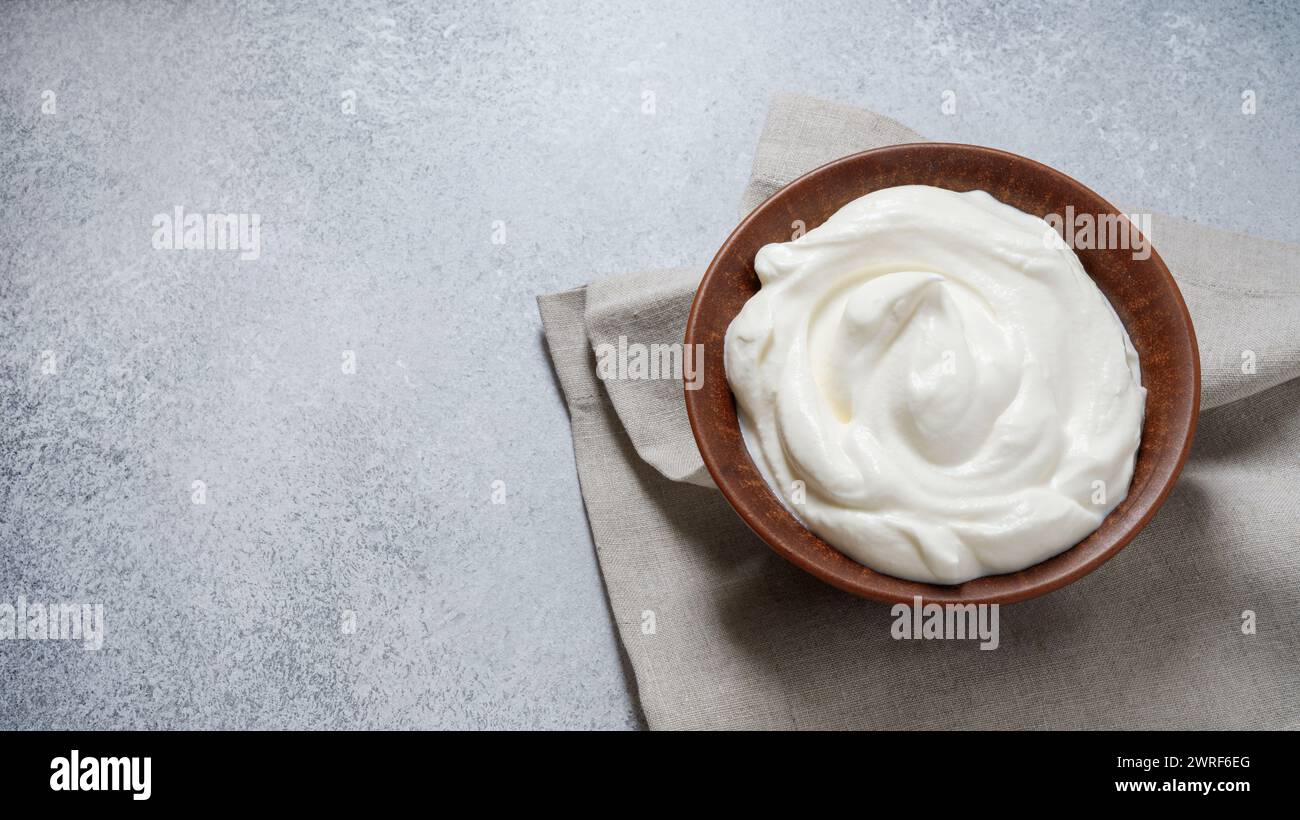 Blick von oben auf Sauerrahm oder Mascarponenkäse in der Keramikschale. Cremige Textur. Kopierbereich. Grauer Betonhintergrund. Stockfoto