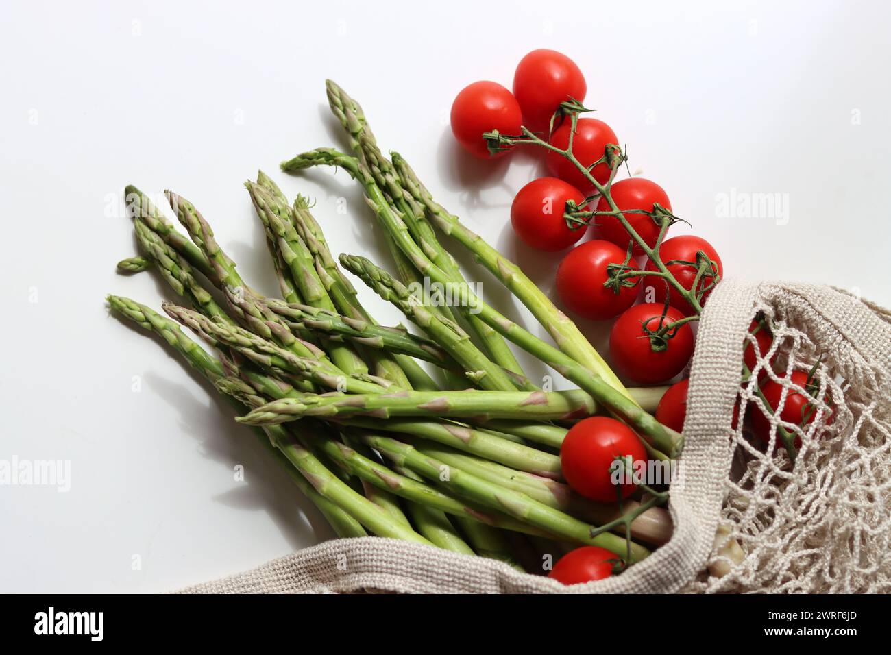 Frische Kirschtomaten und grüner roher Spargel auf weißem Hintergrund mit Kopierraum. Fresh-Konzept. Zutaten für vegetarische Gerichte. Stockfoto