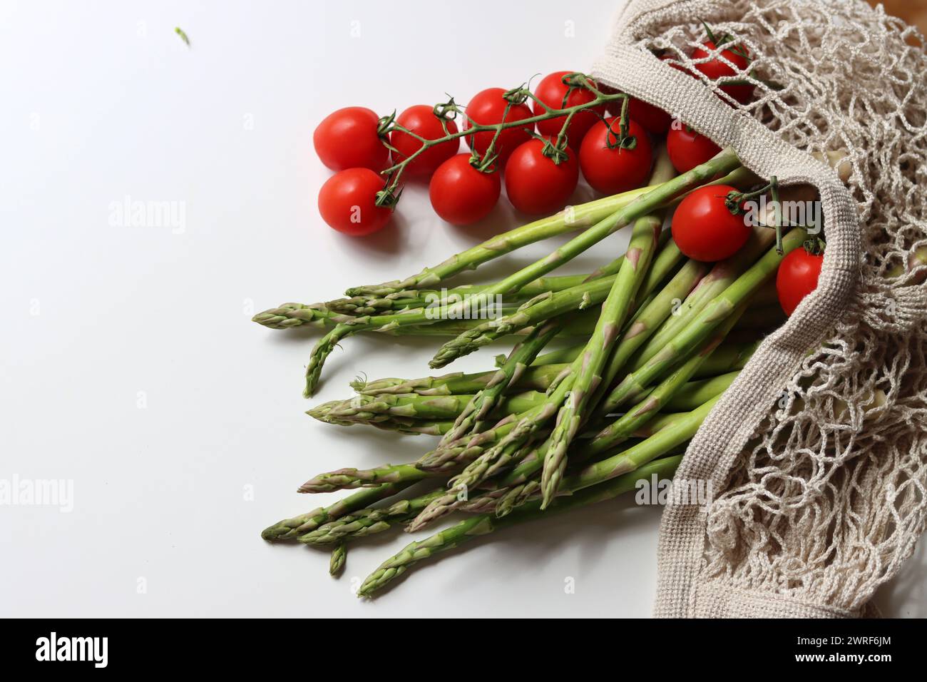 Frische Kirschtomaten und grüner roher Spargel auf weißem Hintergrund mit Kopierraum. Fresh-Konzept. Zutaten für vegetarische Gerichte. Stockfoto