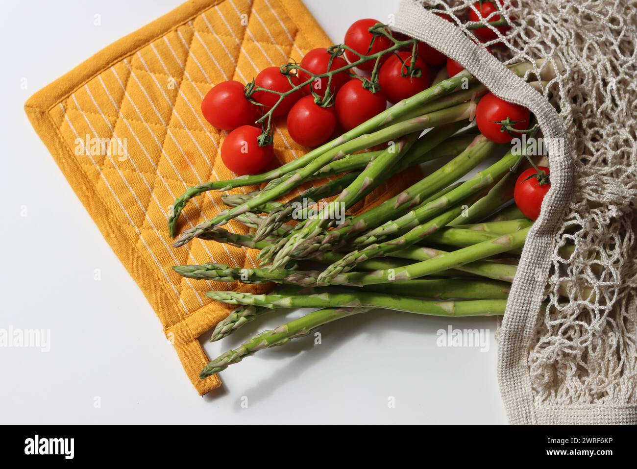 Frische Kirschtomaten und grüner roher Spargel auf weißem Hintergrund mit Kopierraum. Fresh-Konzept. Zutaten für vegetarische Gerichte. Stockfoto