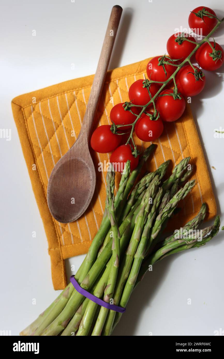 Frische Kirschtomaten und grüner roher Spargel auf weißem Hintergrund mit Kopierraum. Fresh-Konzept. Zutaten für vegetarische Gerichte. Stockfoto