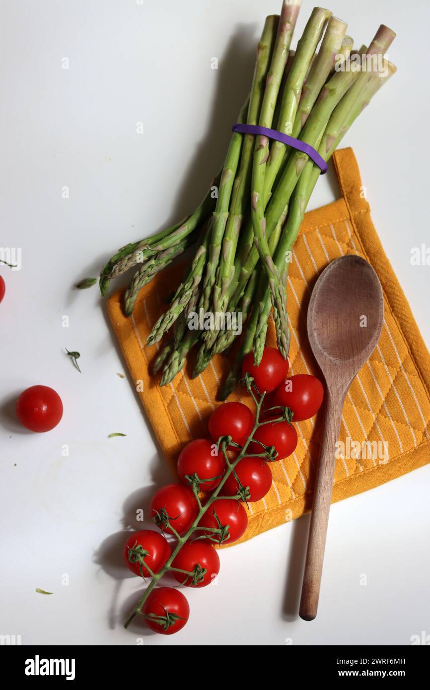 Frische Kirschtomaten und grüner roher Spargel auf weißem Hintergrund mit Kopierraum. Fresh-Konzept. Zutaten für vegetarische Gerichte. Stockfoto
