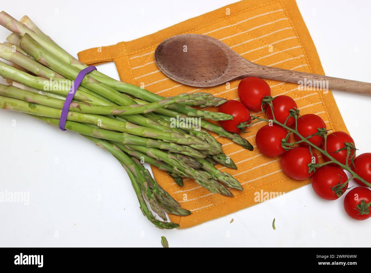 Frische Kirschtomaten und grüner roher Spargel auf weißem Hintergrund mit Kopierraum. Fresh-Konzept. Zutaten für vegetarische Gerichte. Stockfoto