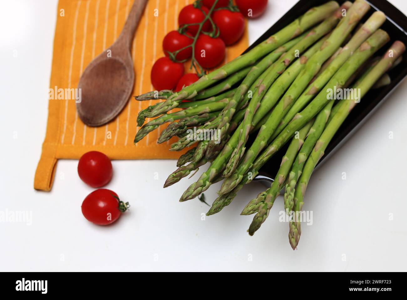 Frische Kirschtomaten und grüner roher Spargel auf weißem Hintergrund mit Kopierraum. Fresh-Konzept. Zutaten für vegetarische Gerichte. Stockfoto