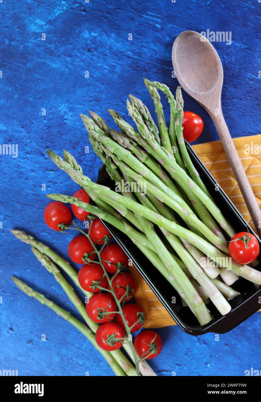 Frischer grüner Spargel und Kirschtomaten auf blau strukturiertem Hintergrund mit Kopierraum. Gesunde Zubereitung des Abendessens. Ausgewogenes Ernährungskonzept. Stockfoto