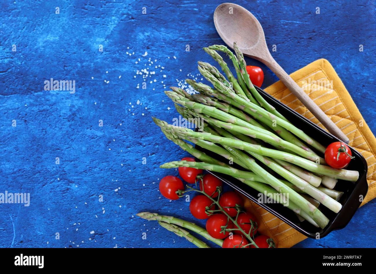 Frischer grüner Spargel und Kirschtomaten auf blau strukturiertem Hintergrund mit Kopierraum. Gesunde Zubereitung des Abendessens. Ausgewogenes Ernährungskonzept. Stockfoto