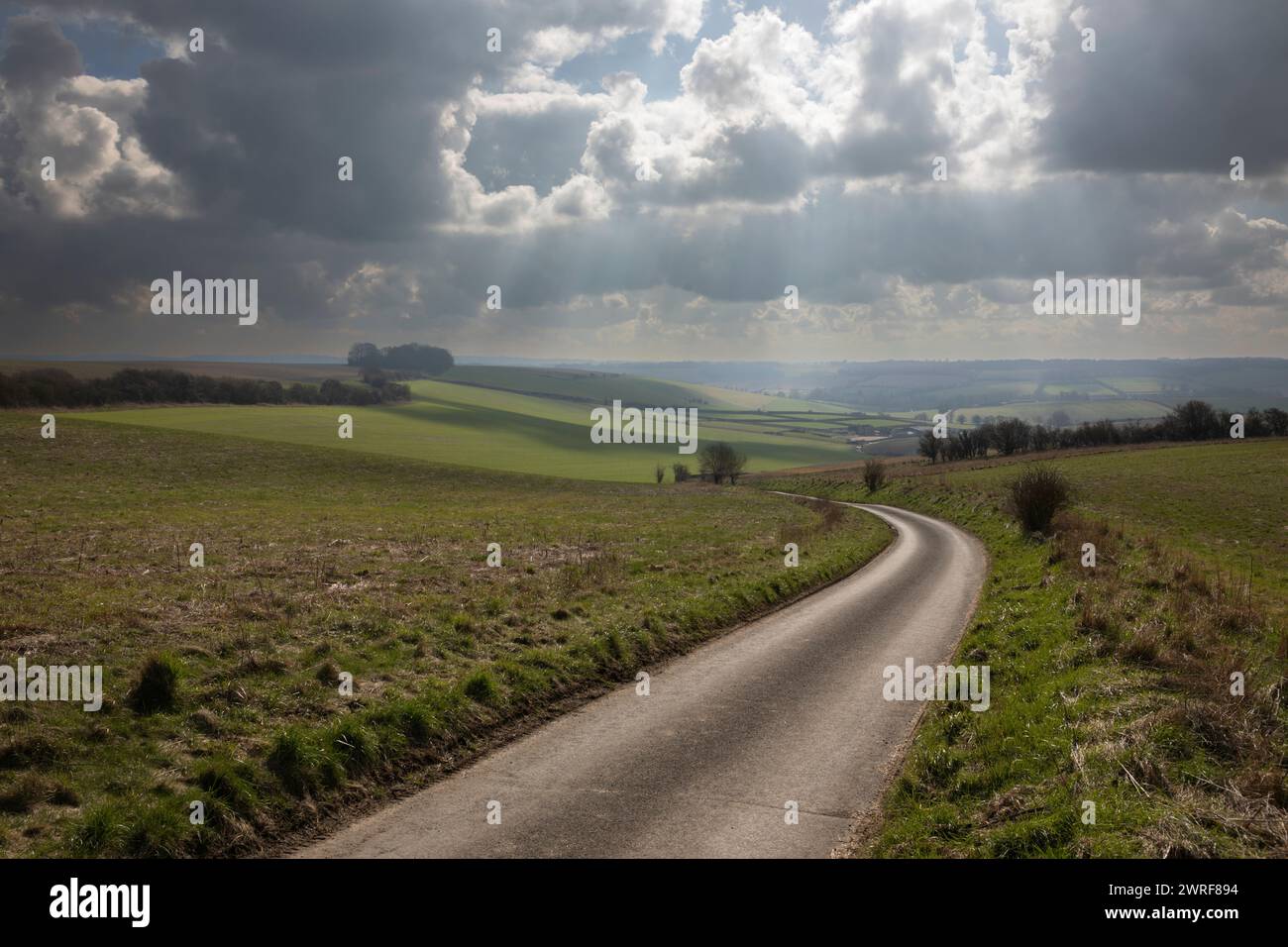 Leere einspurige Landstraße, die durch offenes Ackerland mit dramatischem Himmel hinunter führt, School Lane, East Garston, Berkshire, England, UK Stockfoto