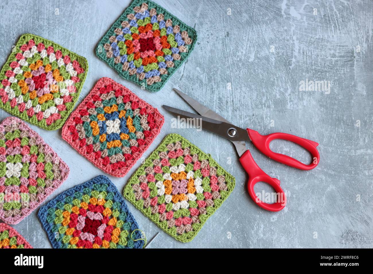 Handgefertigte Zickzackornamente auf grauem Hintergrund mit Kopierraum. Farbenfrohe Baumwoll-Oma-Quadrat. Häkeln Sie die Textur aus der Nähe des Fotos. Stockfoto