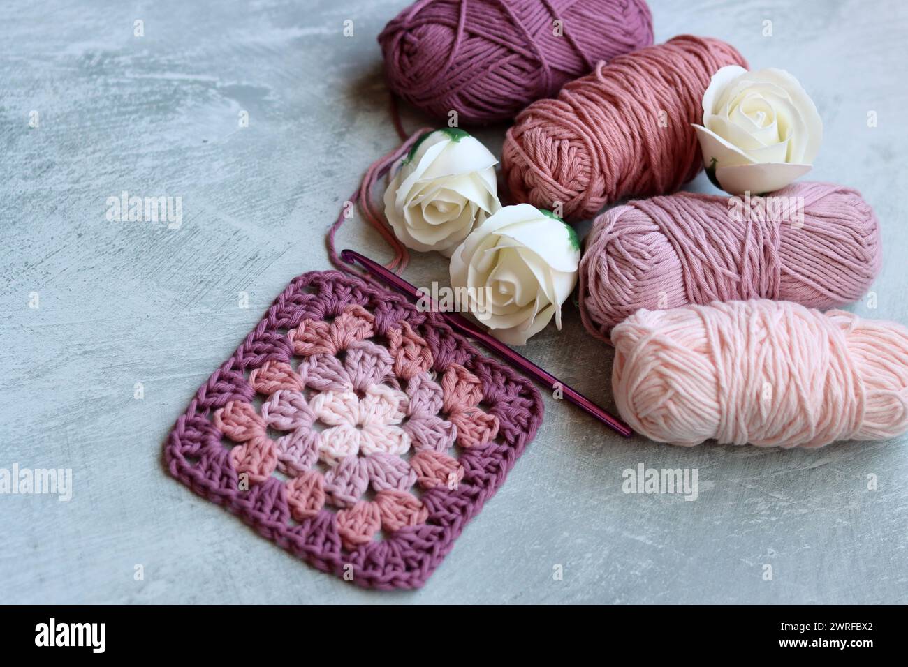 Das Häkelmuster des Granny-Vierecks. Farbenfrohes Foto von weichem rosa Bio-Garn. Hobbys und Freizeitkonzept. Hellgrauer Hintergrund mit Kopierraum. Stockfoto