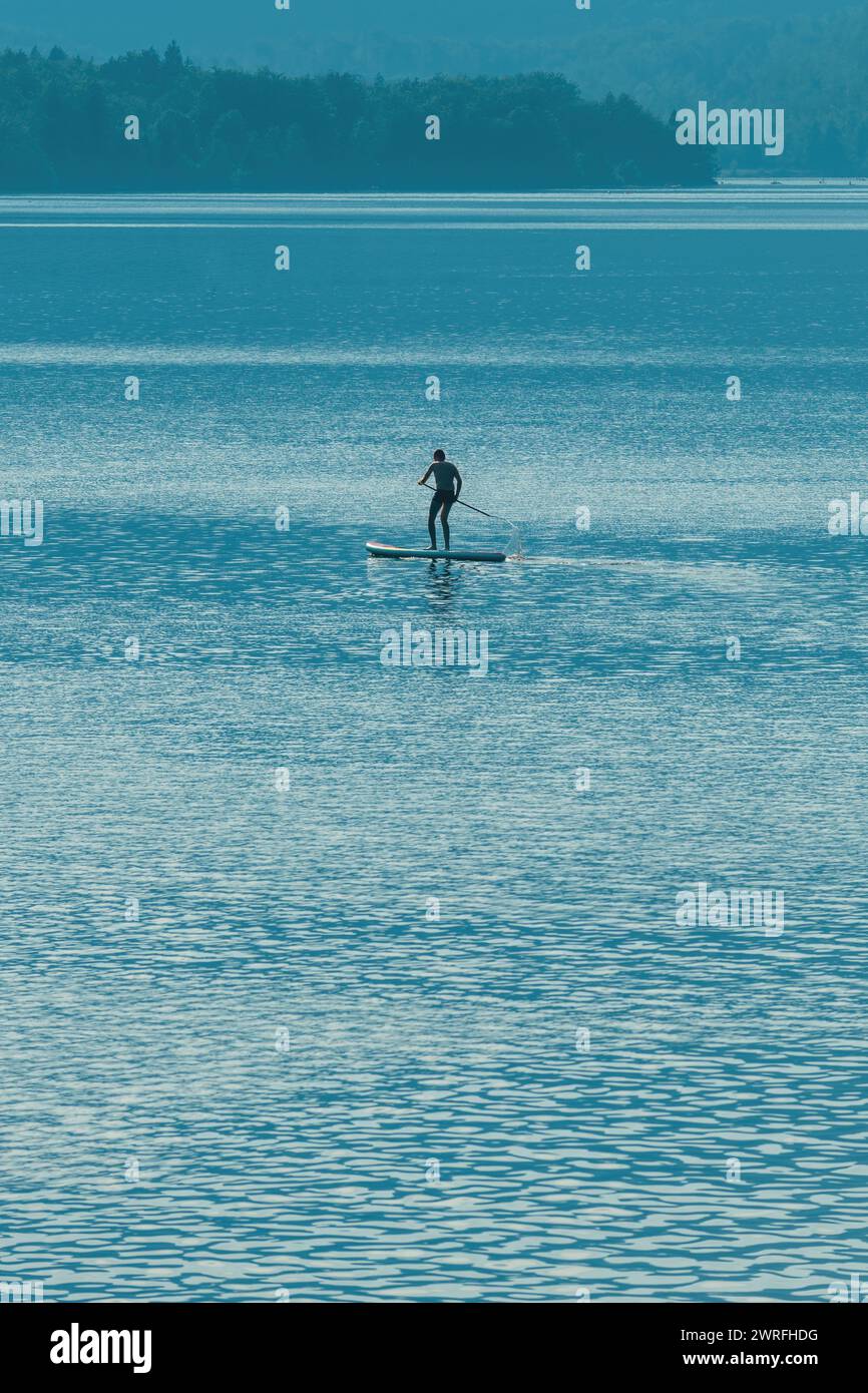 Hinterleuchtete Silhouette eines männlichen Sportlers im Stand-Dup-Board auf dem Bohinj-See in Slowenien, selektiver Fokus Stockfoto